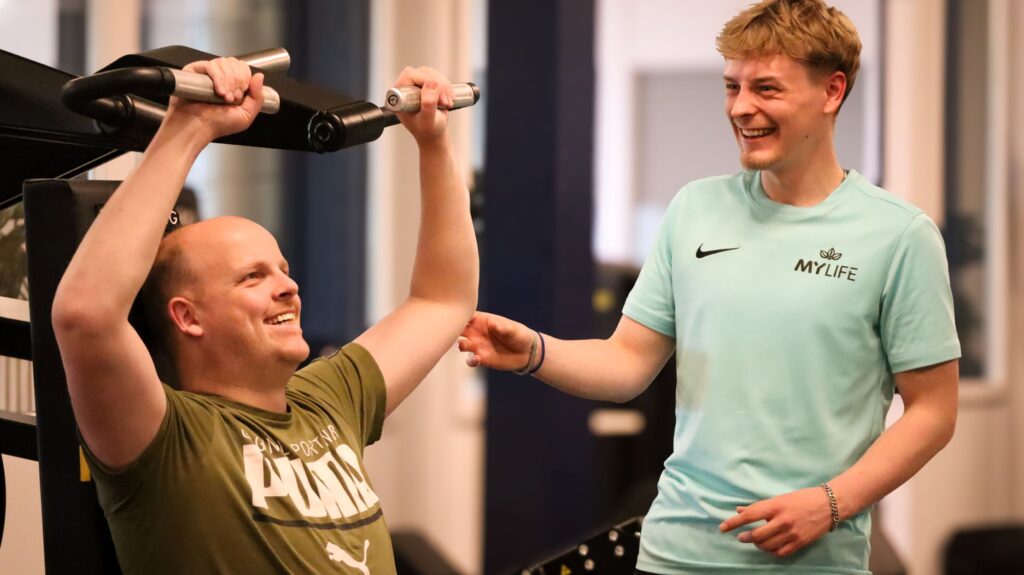 coach begeleidt man op fitnesstoestel